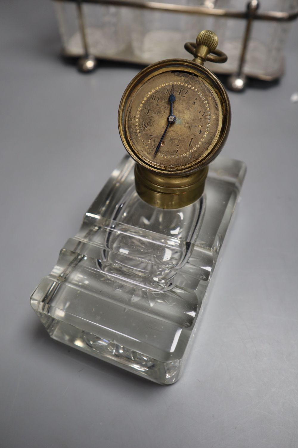 A late 19th century combination desk timepiece / inkwell, hinged timepiece on cut glass well, together with a three decanter tantalus